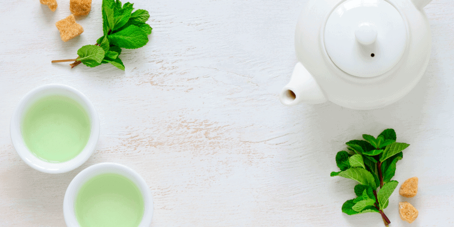 Decorative image of green tea in cups, mint leaves, candied ginger, and a ceramic tea kettle. Herbal iced tea.