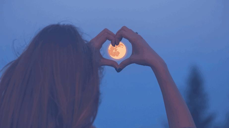 Decorative image of a woman making a heart shape with her hands over the moon in the sky
