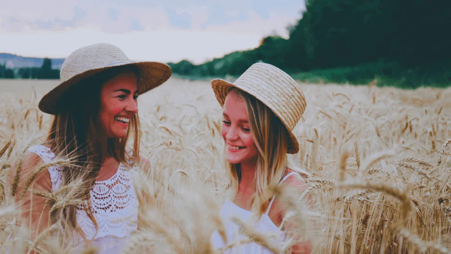 Decorative image of a mother and daughter smiling in a wheat field wearing fancy hats