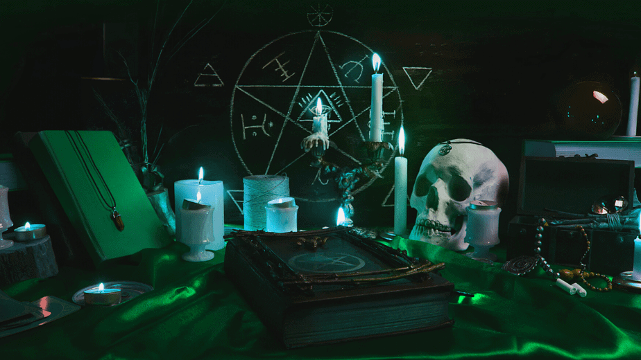 Decorative image of a witch altar with a skull, candles, witch books and more in green