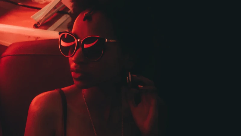 Decorative image of a black woman in sunglasses and red light cast on her