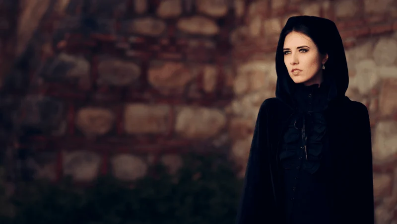 A female witch in a black cloak looking off into the distance