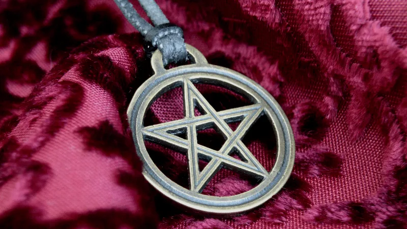A pentacle necklace on leather rope and sitting on purple or red fabric