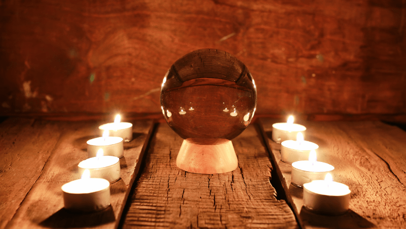Decorative image of a scrying crystal ball between two rows of white tea lights on rustic wood slabs
