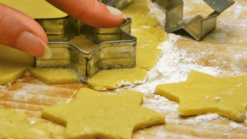 A woman pressing cookie cutters into sugar cookie dough in the shape of stars.