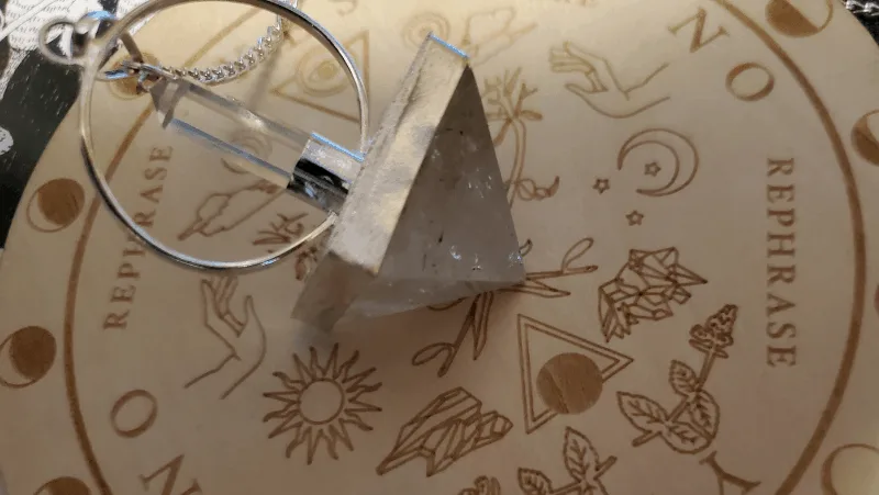 A quartz pendulum pyramid resting on a wooden pendulum board that came in a Tamed Wild box