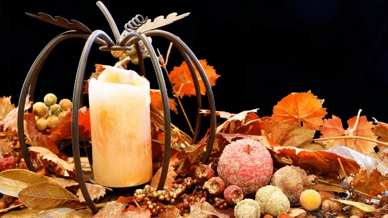A wire metal pumpkin with a candle inside surrounded by candied fruits and fake fall leaves
