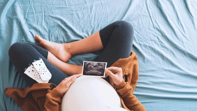 a pregnant woman looking at her ultrasound with cute baby socks in her lap
