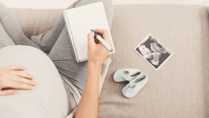A pregnant woman with an ultrasound, baby shoes, and a notebook