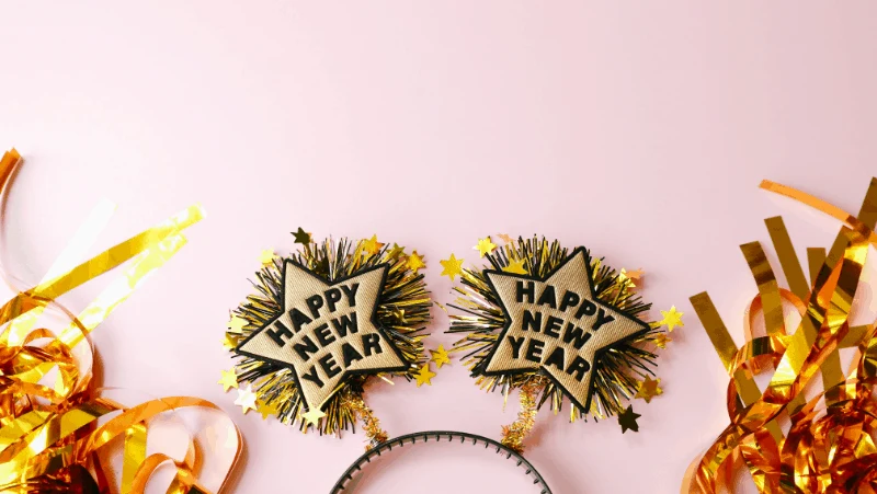 Celebrate new year's eve like a witch. New year's celebration items like headbands and streamers on a pink background.