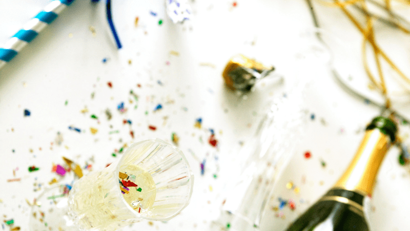 Champagne, glasses, and a mess of confetti on a white background.