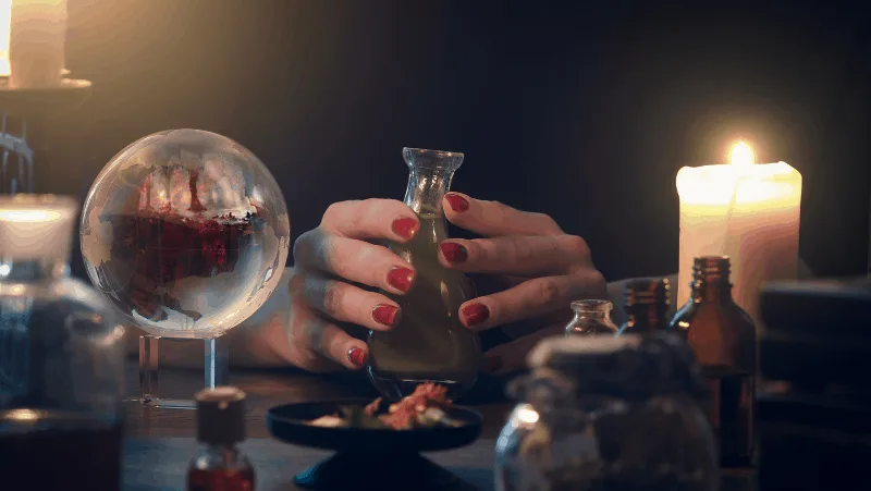 Witchy hands holding a spell jar next to a crystal ball and candle