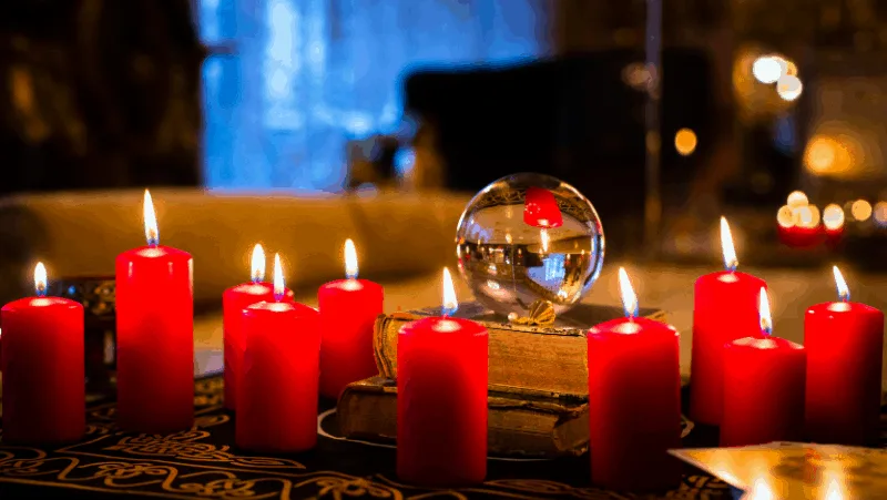 A table with lit red candles, books, and a crystal ball