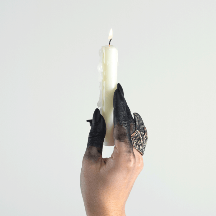 A witchy hand with scorched black fingers holding a white candle for Imbolc