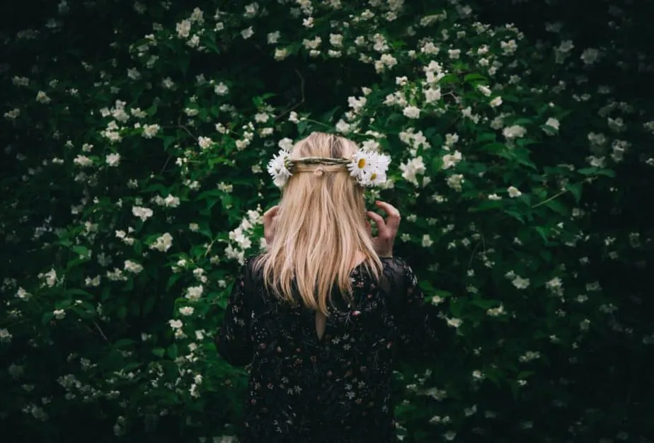 A swedish girl standing infront of a jasmine flower bush. In her hair she has a swedish midsummer wreath.