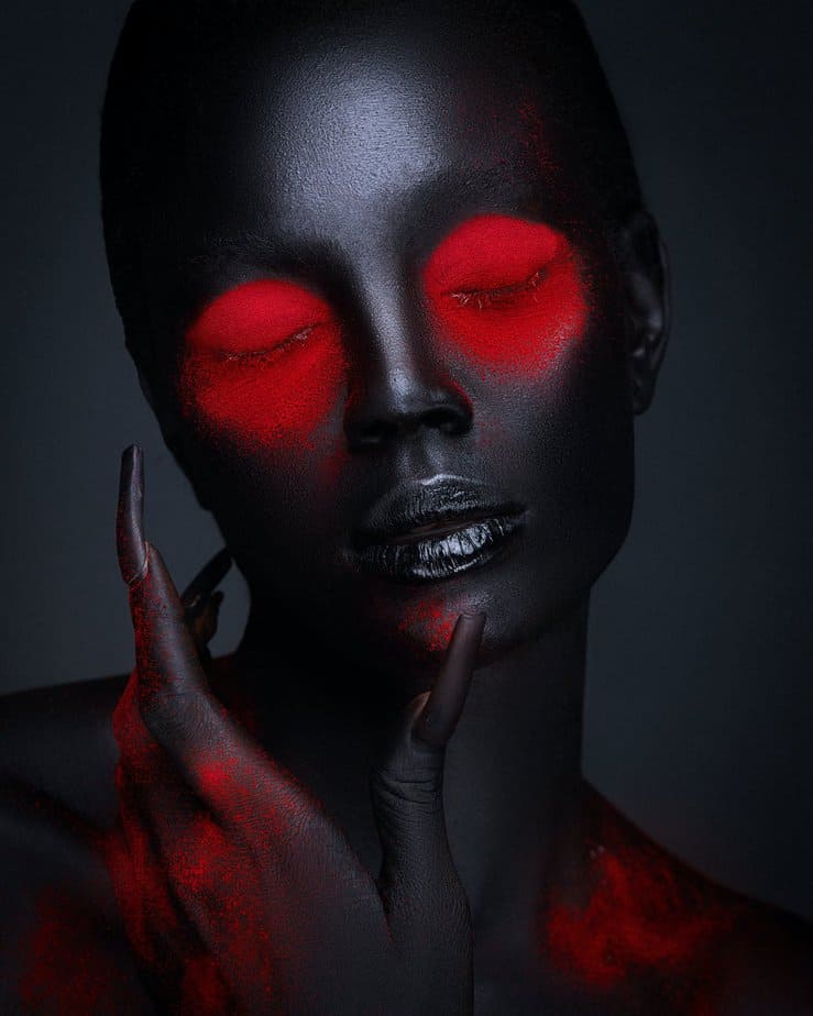 black painted female face with red creative diabolic makeup and manicure
