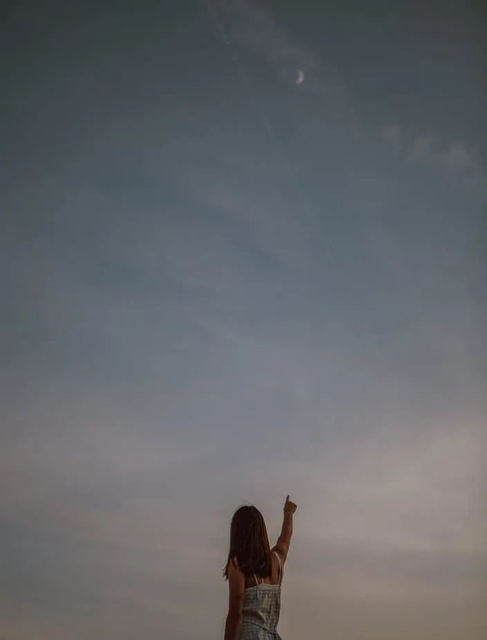 woman pointing at sunset sky in evening