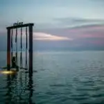 faceless traveler on swing in sea at sunset