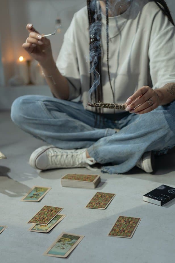 woman sitting on the floor beside tarot cards and burning herbs