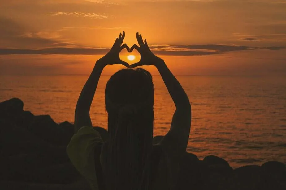 silhouette of woman doing heart sign during sunset