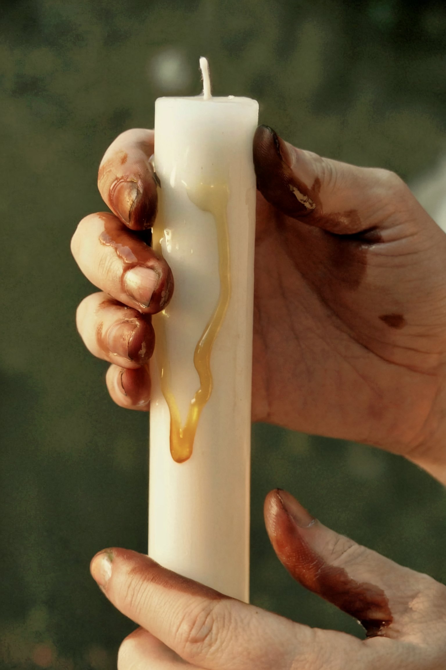 Hand holding white pillar candle with golden honey and oil dripping down surface during Yule anointing preparation