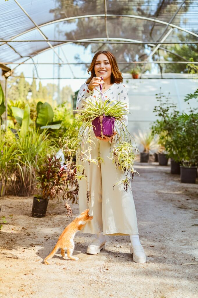 a woman standing in a greenhouse with a cat