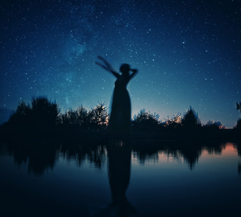 silhouette of woman standing on rock near body of water during night time