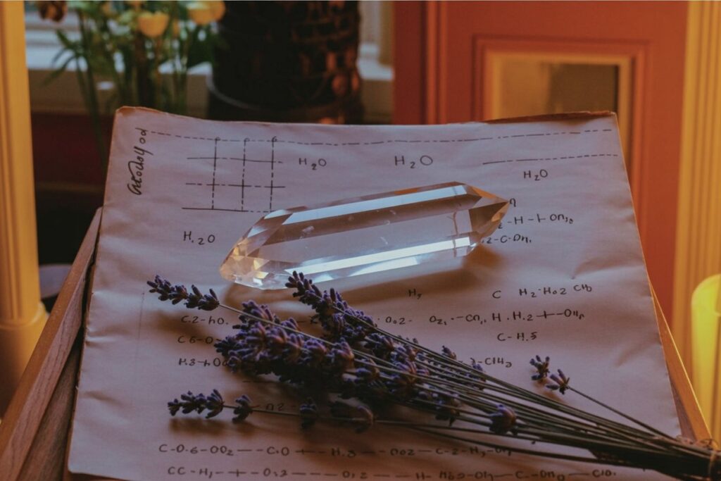The crystal gives your hands something to hold so your mind can settle on the work. Lavender scattered across your notes does two things: smells good and drops cortisol within minutes. Those H₂O formulas on the paper show the actual chemistry behind why herb magic works. Your hippocampus (the memory-making part of your brain) physically shrinks under stress. Lavender stops that. Crystal plus scent plus written formulas equals your brain in the best possible state to learn.