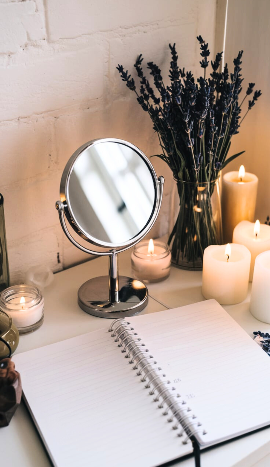 A simple silver mirror is placed on a table with glowing candles, a vase of lavender, and an open planner. Highlights holistic morning routine ideas and wellness morning routines for self-care activities. Ideal for setting up your day for success with positive morning affirmations and inspirational quotes.
