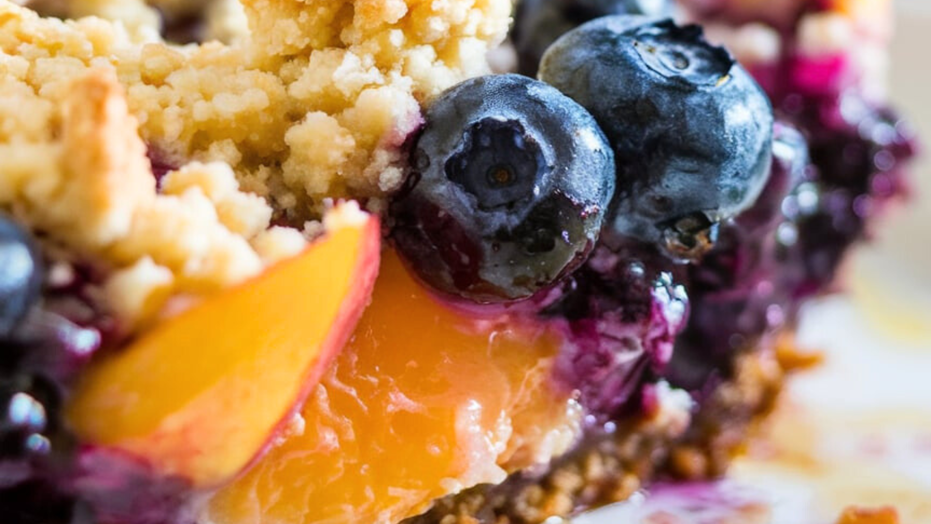 Modern peach crisp with ice cream A close-up of a Peach and Blueberry Crisp, showcasing golden, crumbly oat topping with juicy blueberries and peach slices glistening beneath. The blueberries are plump and bursting, while the peaches have a soft, sunlit orange hue. The texture of the crust and the fruit's glossy juices create a hyperrealistic, mouthwatering visual.