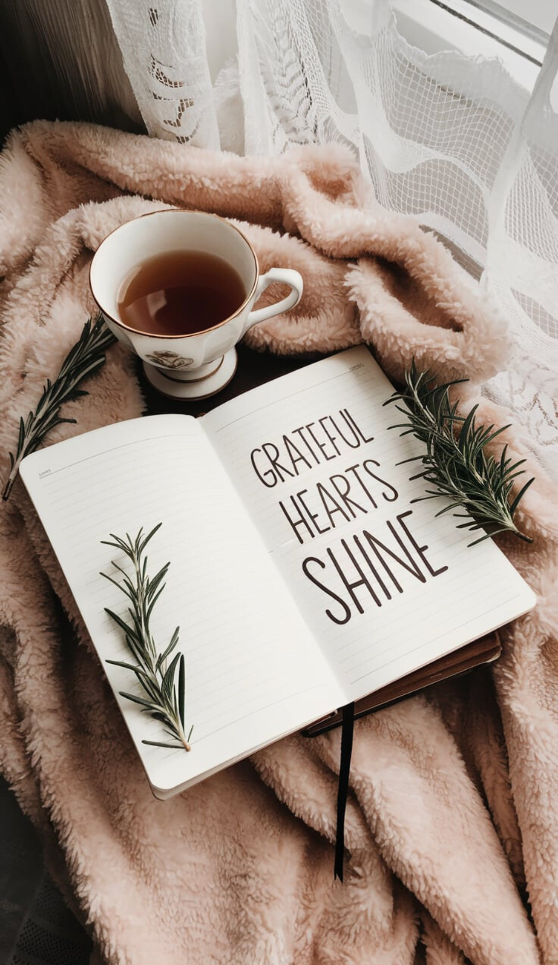 A cozy setup with a gratitude journal, a steaming cup of tea, sprigs of rosemary, and a soft blanket. Text reads 'Grateful Hearts Shine.' Captures the essence of a positive morning, self-care activities, and inspirational affirmations for a heart-centered start to the day.