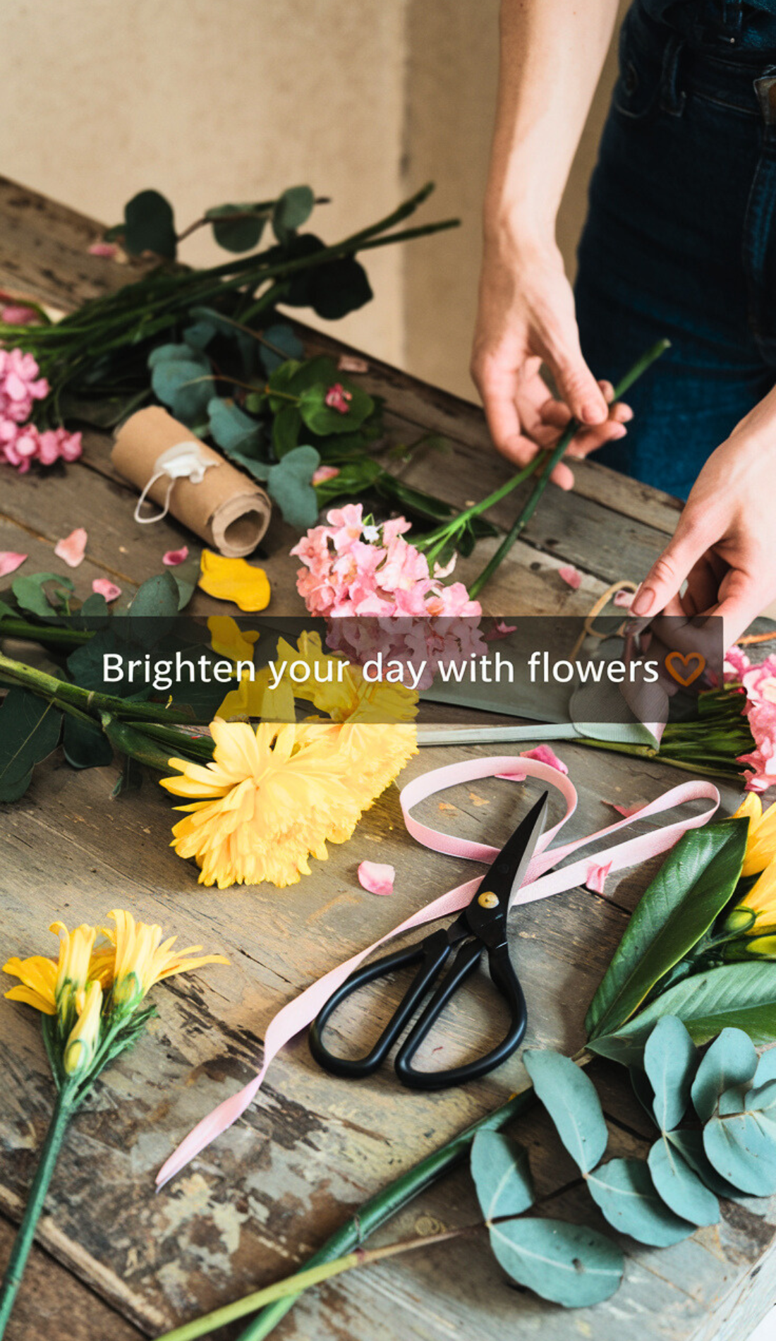 Hands arranging fresh flowers like yellow daisies and pink roses on a rustic table with scissors and ribbon. Represents morning ritual ideas for energizing morning routines and inspiring productivity. Perfect for a healthy girl lifestyle and creating vision board photos for positive mornings.