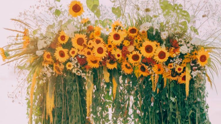 Floral Litha wedding ideas A lush, cascading wedding altar made of sunflowers, wild greenery, and delicate white flowers creates a radiant focal point. Golden wheat stalks and hanging floral elements add a natural, bohemian touch.