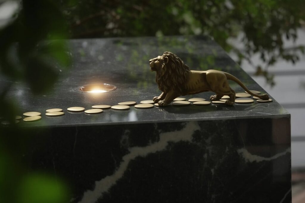 The North Node in Leo demands solar authority but the Sun in Pisces has to earn it through years of systematic work Bronze lion statue in crouching stance on black marble pedestal with natural gray veining, twelve golden coins arranged in curved upward path