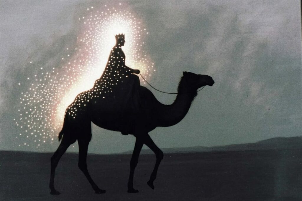 Black silhouette of crowned figure riding camel in profile against misty gray background with sparkling white light around crown and rolling hills in distance